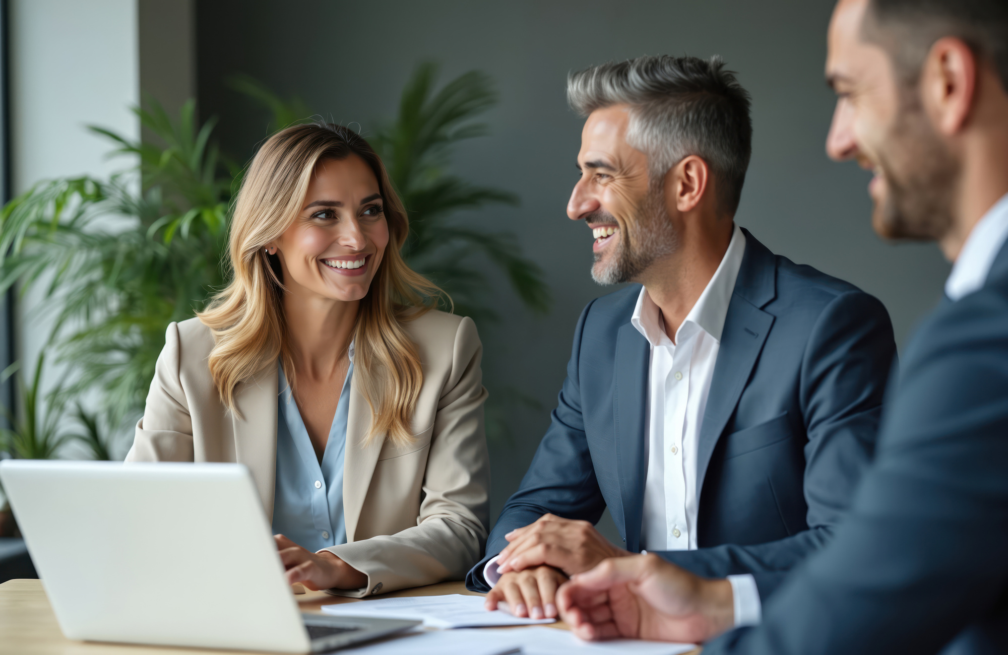 Smiling business people, colleagues, executives in suits at meeting. Teamwork, partnership, discussion, using laptop in modern office. Happy, positive atmosphere, corporate environment, success.