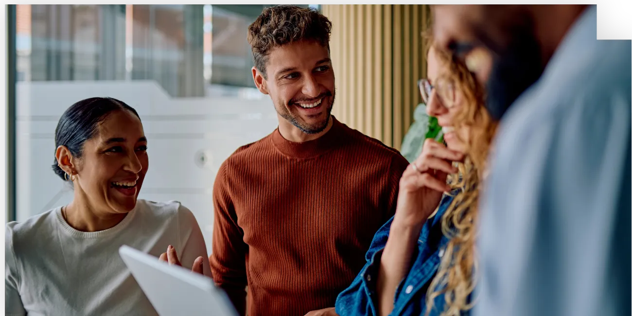 Four colleagues smiling and discussing work around a tablet-converted-from-png